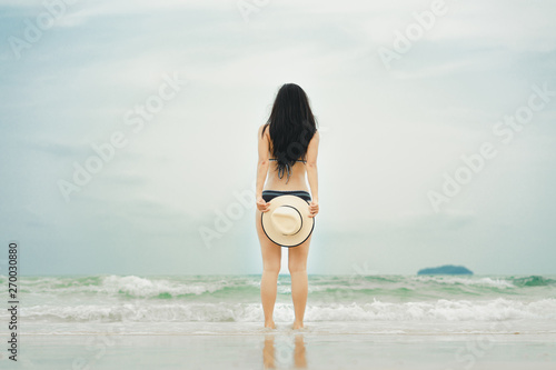 Asian woman in bikini with straw hat standing on the tropical beach in summer holiday