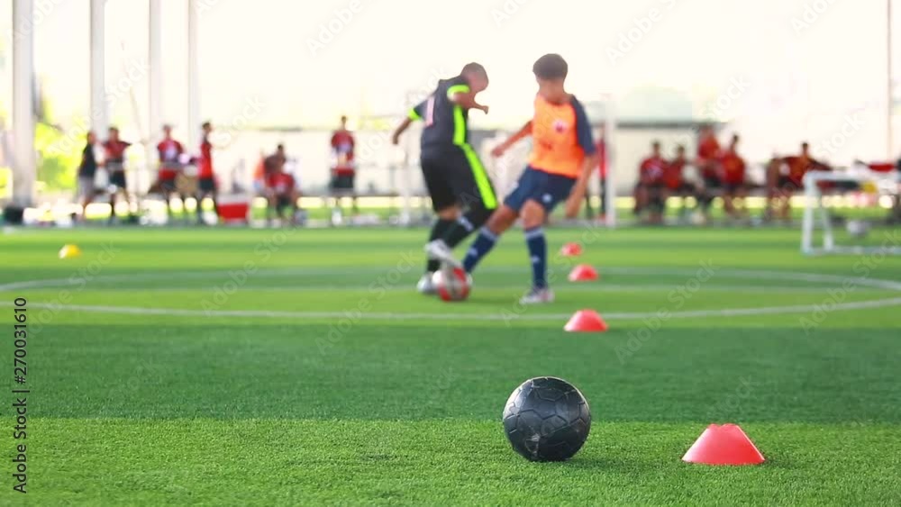 black football on green artificial turf with marker cone blurry soccer team training, blurry boy soccer player jogging between marker cones and control ball with soccer equipment in soccer academy. black football on green artificial turf with marker cone blurry soccer team training, blurry boy soccer player jogging between marker cones and control ball with soccer equipment in soccer academy.