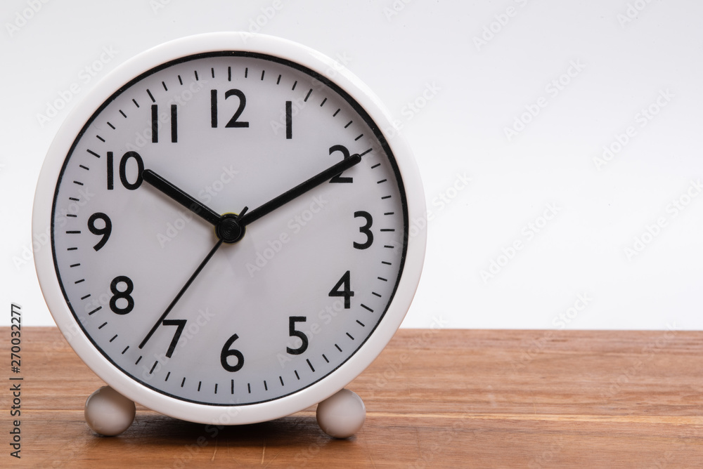 White alarm clock on a wooden table isolated in white background White alarm clock on a wooden table isolated in white background