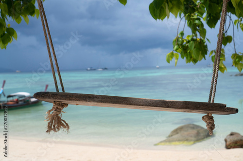 Swing hang from tree over beautiful tropical island view with boats on the sea and sky background. Exotic vacation on Amazing Koh Lipe in Thailand photo