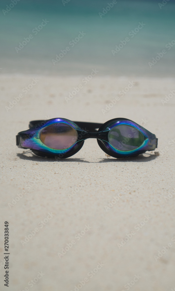 Swim goggles on sandy beach over lagoon sea background. Travel, holiday, tropical vacation concept