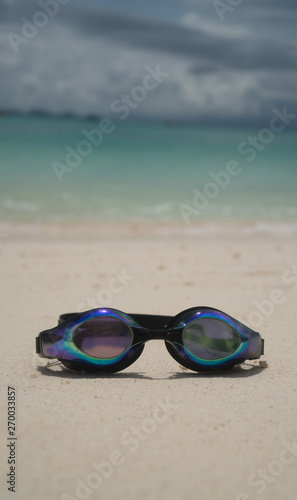 Swim goggles on sandy beach over lagoon sea background. Travel, holiday, tropical vacation concept