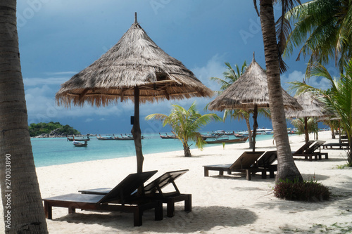 Fototapeta Naklejka Na Ścianę i Meble -  Amazing tropical beach with deckchairs, umbrella, palm trees over lagoon sea with boats. Tropical vacation, holiday, travel concept