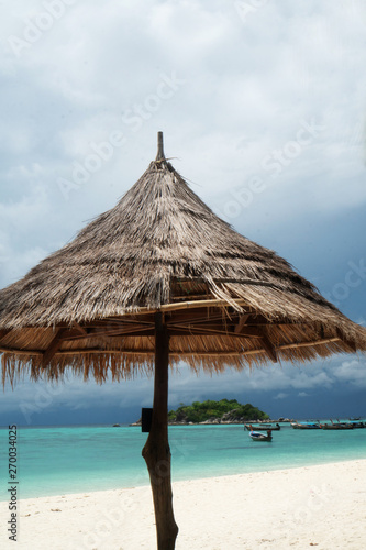 Umbrella on beautiful sandy beach over lagoon sea water with boats and small green island. Amazing exotic Koh lipe island in Thailand. Tropical vacation  holiday  travel concept