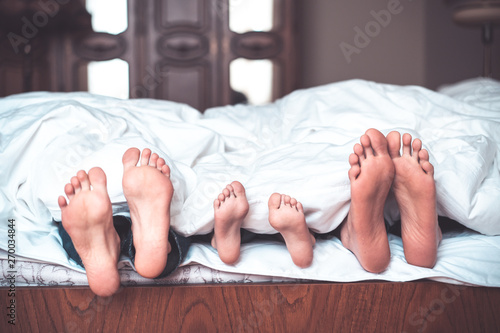 happy family of three is lying on the bed and only feet seen