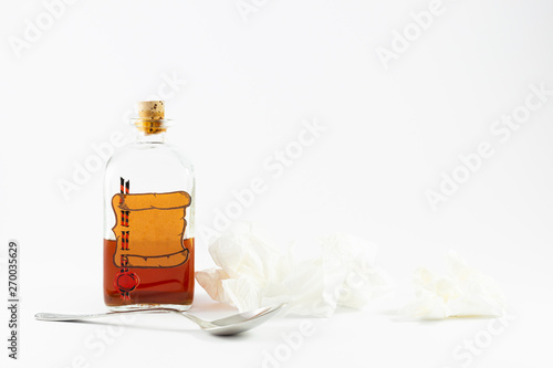 Arrangement of a spoon, handkerchiefs and a vintage medicine bottle with cork filled with orange liquid and furnished with an empty label like a parchment roll with red sealing wax on white background