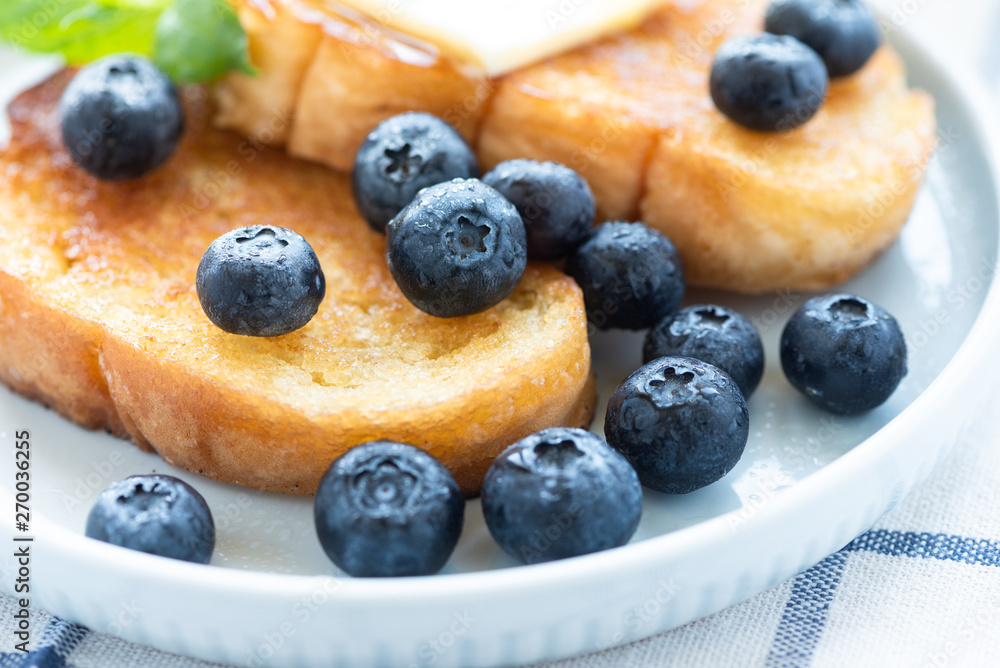 Fototapeta premium French toast with blueberries, honey and butter on a light plate. Sweet country breakfast.