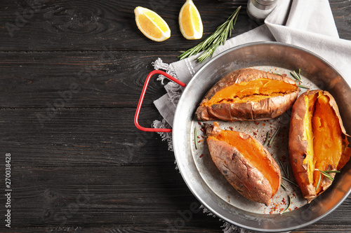 Flat lay composition with baked sweet potatoes in dish on wooden background. Space for text