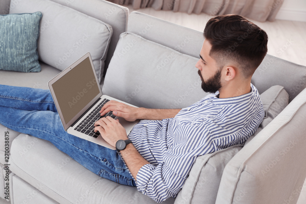 Handsome young man working with laptop on sofa at home Handsome young man working with laptop on sofa at home