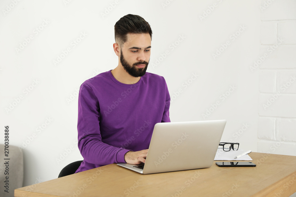 Handsome young man working with laptop at table in home office Handsome young man working with laptop at table in home office