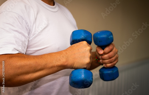 Adult man doing exercise in the gym. Man with small blue weights. Health and wellness concept.