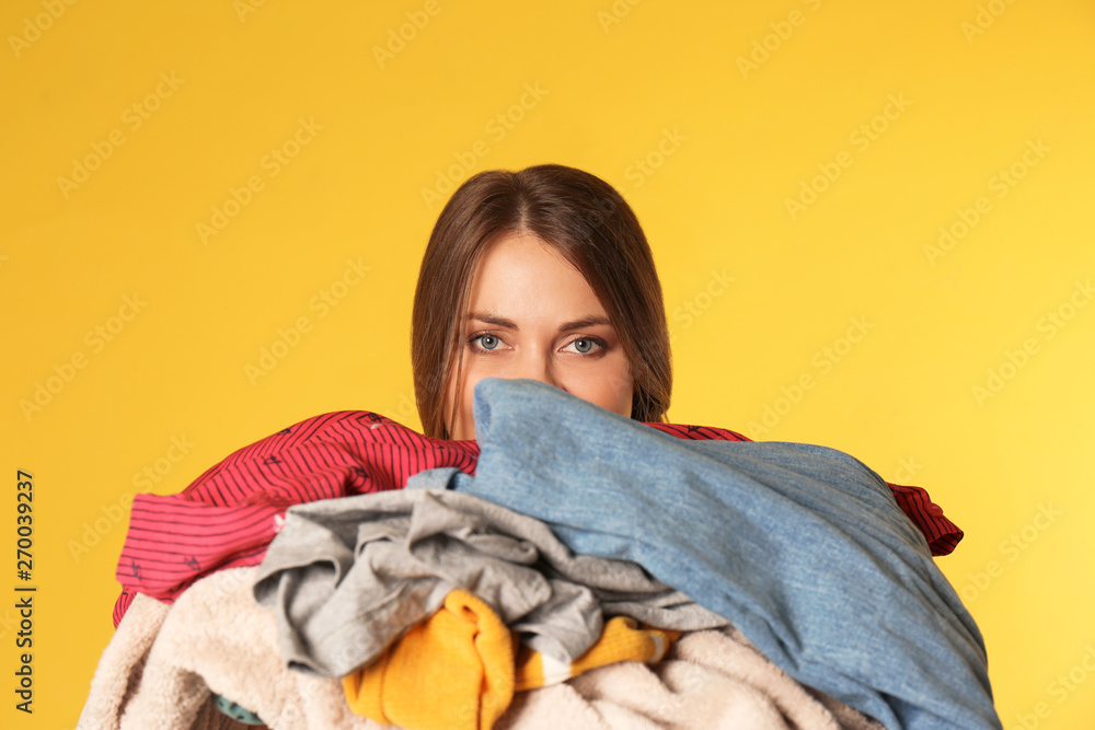 Young woman holding pile of dirty laundry on color background