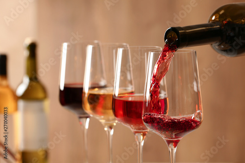 Fototapet Pouring wine from bottle into glass on blurred background, closeup