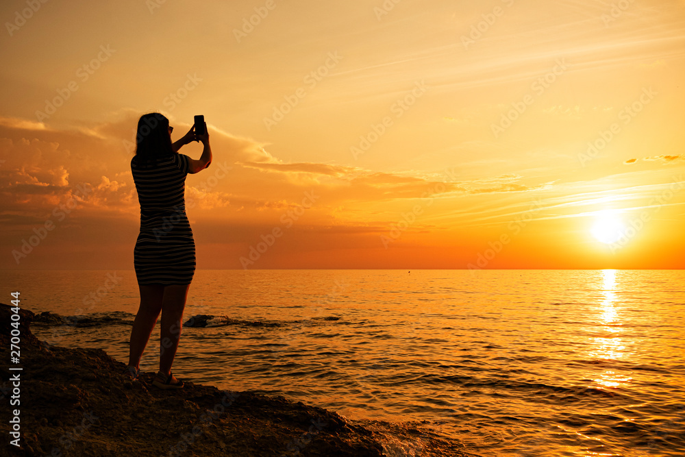 silhouette of a young girl. Photographs a beautiful sunset on the phone.