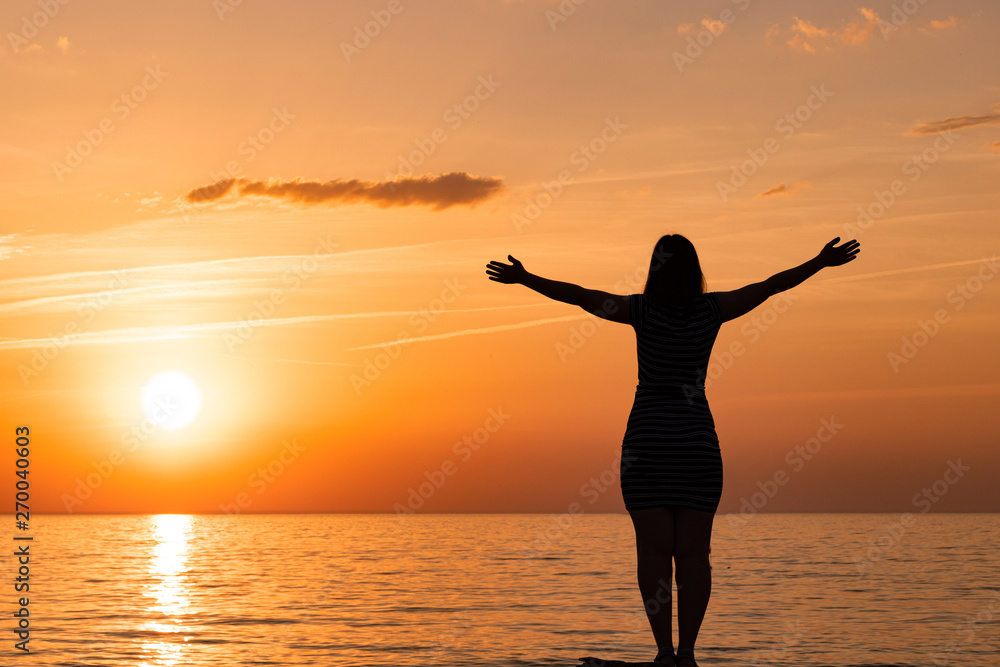 silhouette of a young girl. standing in a pose with arms at sunset.