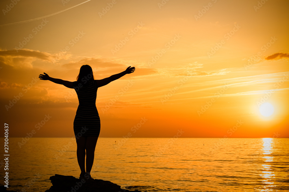 silhouette of a young girl. standing in a pose with arms at sunset.