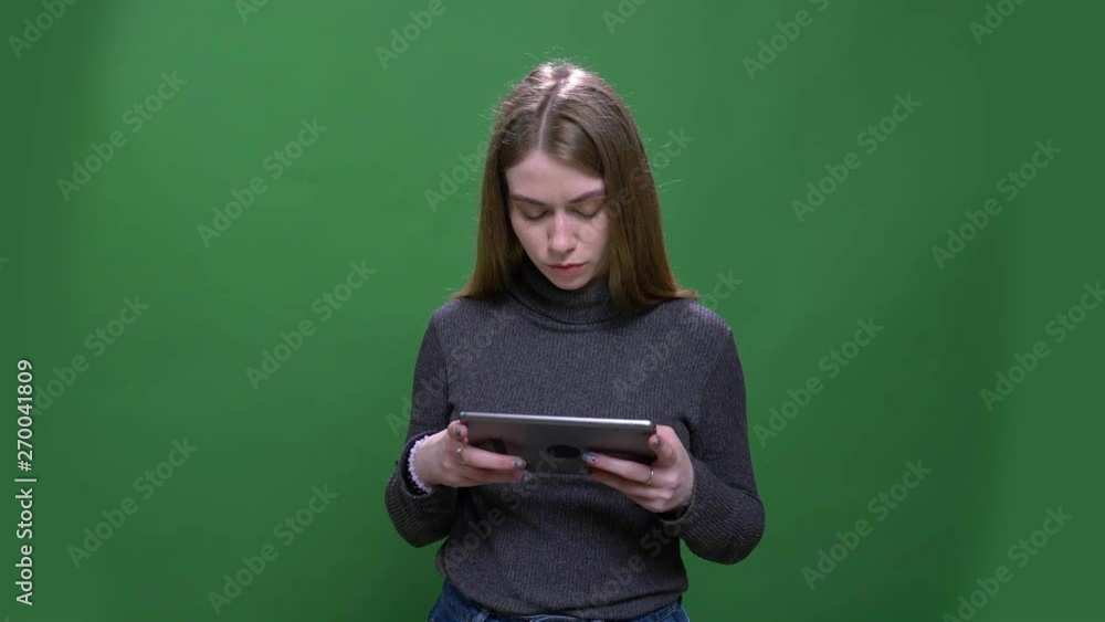 Young blonde businesswoman working attentively with tablet isolated on green chromakey background. Young blonde businesswoman working attentively with tablet isolated on green chromakey background.