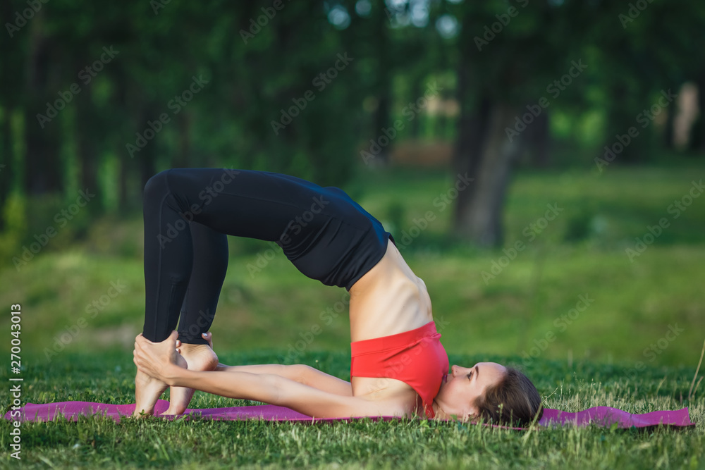 Fototapeta premium Young woman doing yoga exercises in the summer city park. Health lifestyle concept.