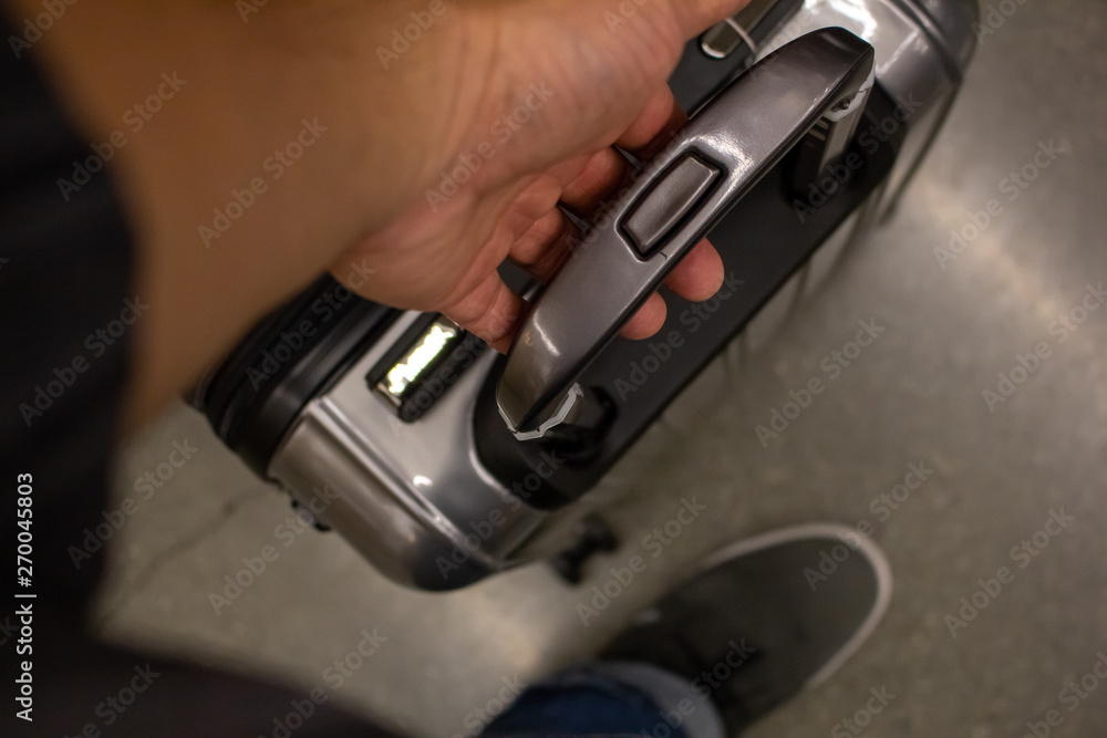 A hand holds onto a rolling compact suitcase at the airport A hand holds onto a rolling compact suitcase at the airport