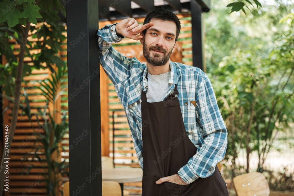 Obraz premium Portrait of young barista man smiling at camera while working in street cafe or coffeehouse outdoor