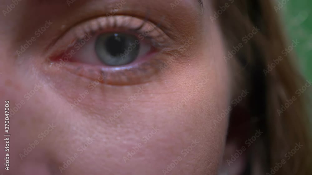 Close-up one eye portrait of blonde model watches calmly and intently into camera on green chromakey background. Close-up one eye portrait of blonde model watches calmly and intently into camera on green chromakey background.