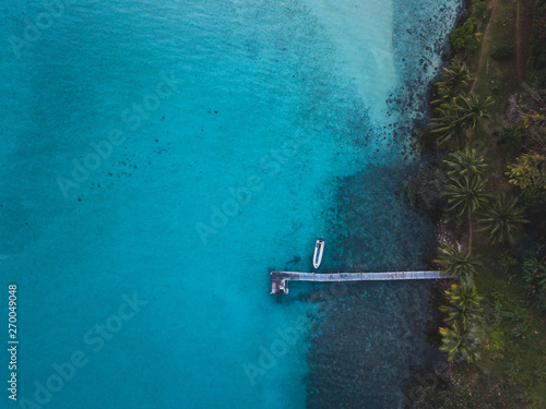 aerial landscape of tropical island and wooden pier with boat, top down view of blue water and palm trees from drone