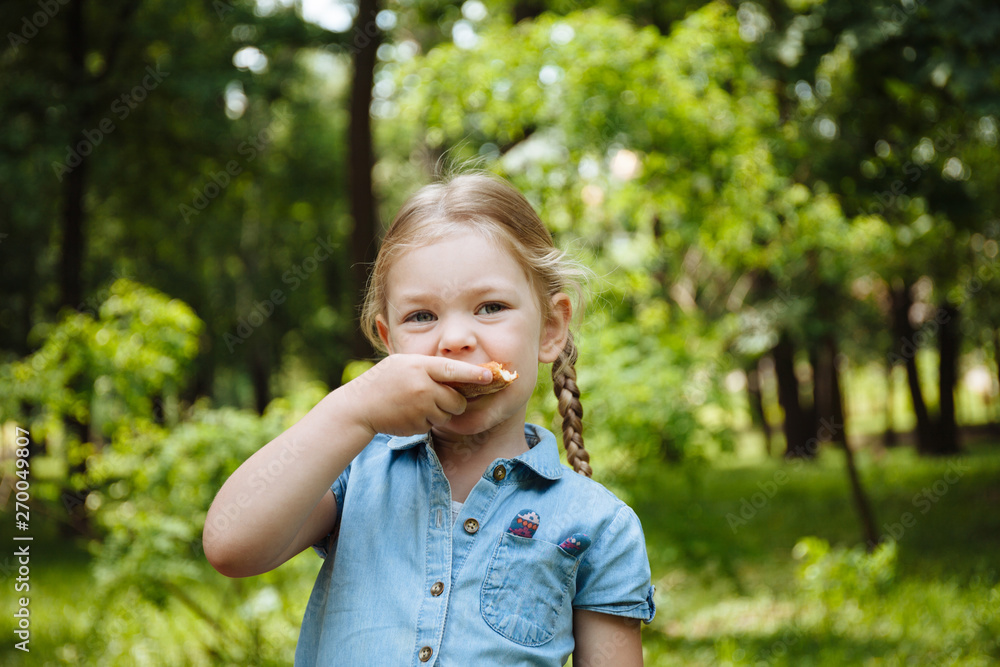 Little baby girl eating pizza and laughing outdoors on the background of green grass, summer picnic. Rest in the park. Little baby girl eating pizza and laughing outdoors on the background of green grass, summer picnic. Rest in the park.