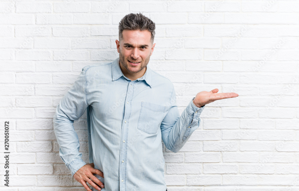 Young handsome man against a bricks wall showing a copy space on a palm and holding another hand on waist. Young handsome man against a bricks wall showing a copy space on a palm and holding another hand on waist.