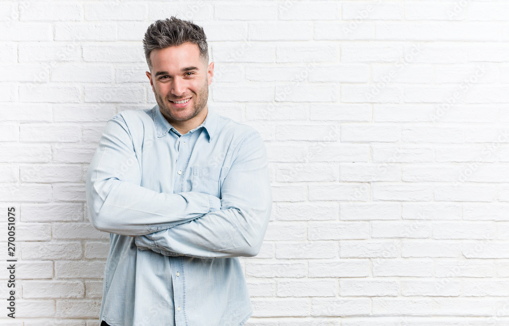 Young handsome man against a bricks wall who feels confident, crossing arms with determination. Young handsome man against a bricks wall who feels confident, crossing arms with determination.