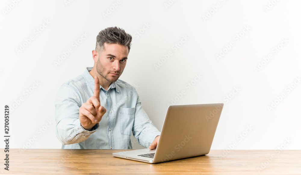 Young handsome man working with his laptop showing number one with finger. Young handsome man working with his laptop showing number one with finger.