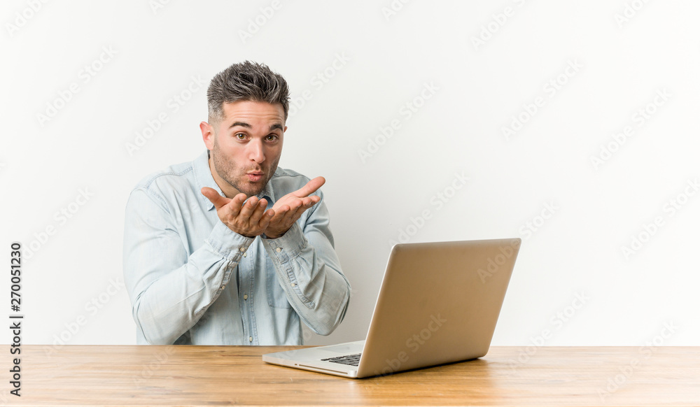Young handsome man working with his laptop folding lips and holding palms to send air kiss. Young handsome man working with his laptop folding lips and holding palms to send air kiss.