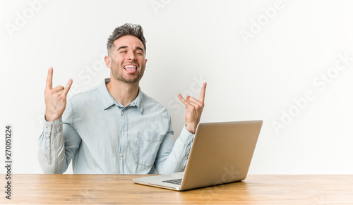 Young handsome man working with his laptop showing rock gesture with fingers