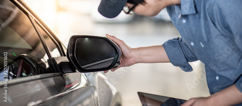 Young Asian auto mechanic holding digital tablet checking car wing mirror. Mechanical maintenance engineer working in automotive industry. Automobile servicing and repair concept