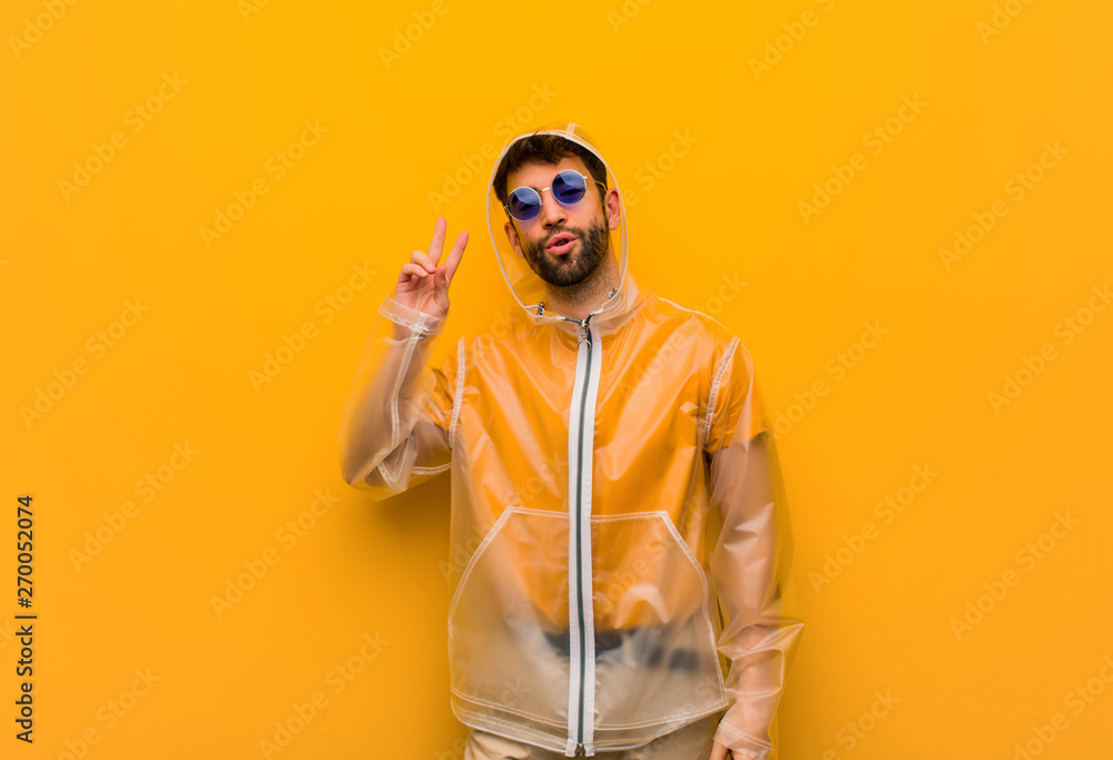 Young man wearing a rain coat fun and happy doing a gesture of victory Young man wearing a rain coat fun and happy doing a gesture of victory