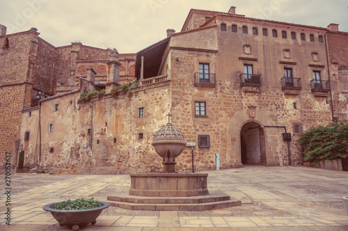 Fountain in square encircled by gothic buildings with gateway arch at Plasencia