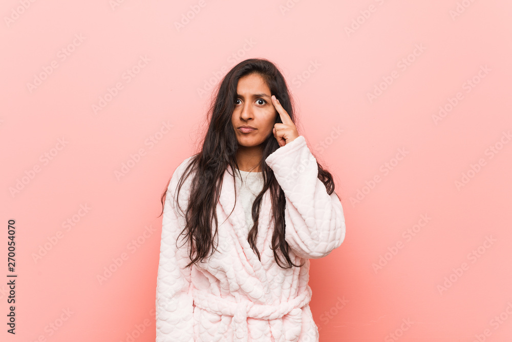 Young indian woman wearing pajama pointing temple with finger, thinking, focused on a task. Young indian woman wearing pajama pointing temple with finger, thinking, focused on a task.