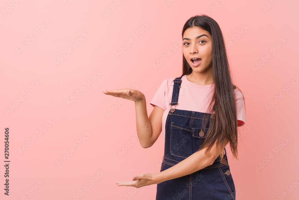 Young pretty arab woman wearing a jeans dungaree shocked and amazed holding a copy space between hands. Young pretty arab woman wearing a jeans dungaree shocked and amazed holding a copy space between hands.