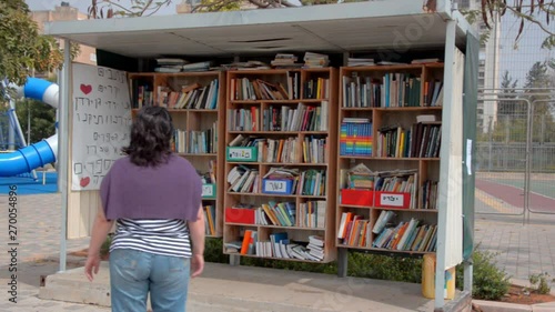 Woman walking down Hoshen Street, comes to the street library and picks up a book for herself. The books are free to borrow and can either be returned or exchanged. Taken in Ness Ziona, Israel