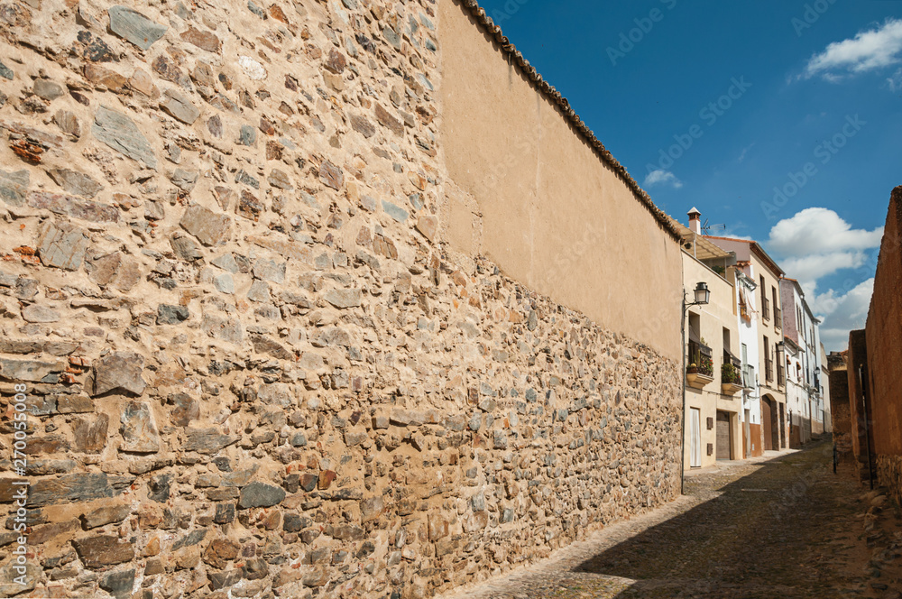 Rough stone wall in narrow alley with old houses at Caceres