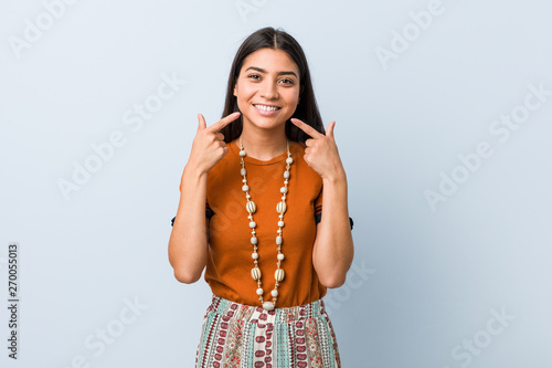 Young arab woman smiles, pointing fingers at mouth.