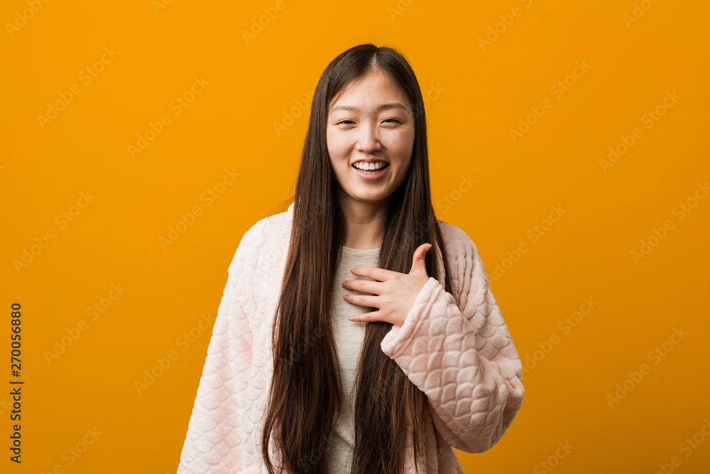 Young chinese woman in pajama laughs out loudly keeping hand on chest. Young chinese woman in pajama laughs out loudly keeping hand on chest.