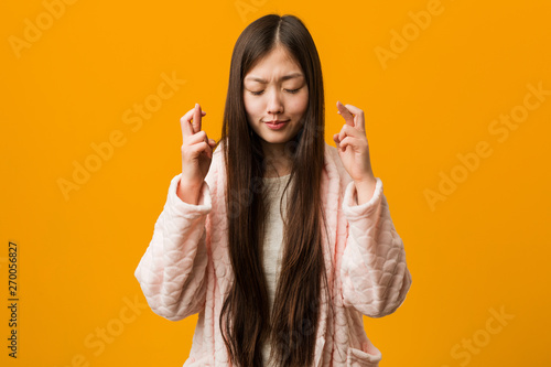 Young chinese woman in pajama crossing fingers for having luck photo