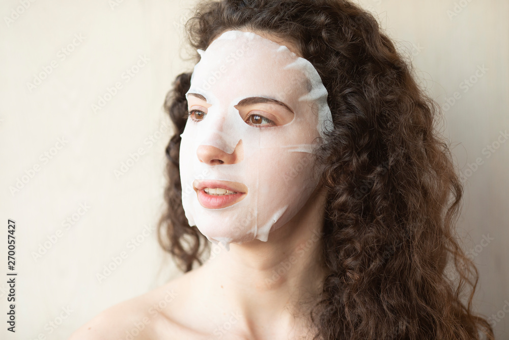 Beautiful young woman with naked shoulders posing at grey background with facial mask, skin care concept, beauty photo, skin treatment, spa procedure Beautiful young woman with naked shoulders posing at grey background with facial mask, skin care concept, beauty photo, skin treatment, spa procedure