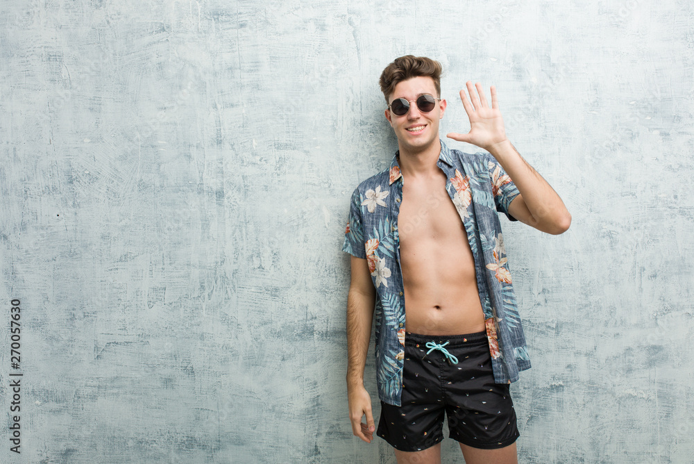 Young caucasian man wearing a swimsuit smiling cheerful showing number five with fingers.