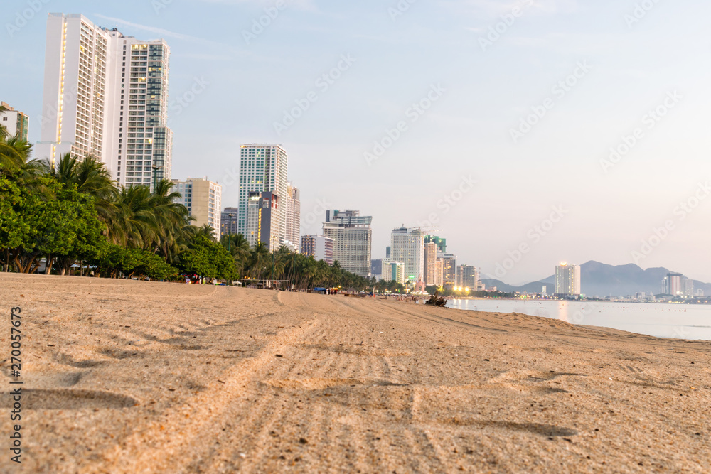 Beach with tropical trees on shore and tall building at dawn Beach with tropical trees on shore and tall building at dawn