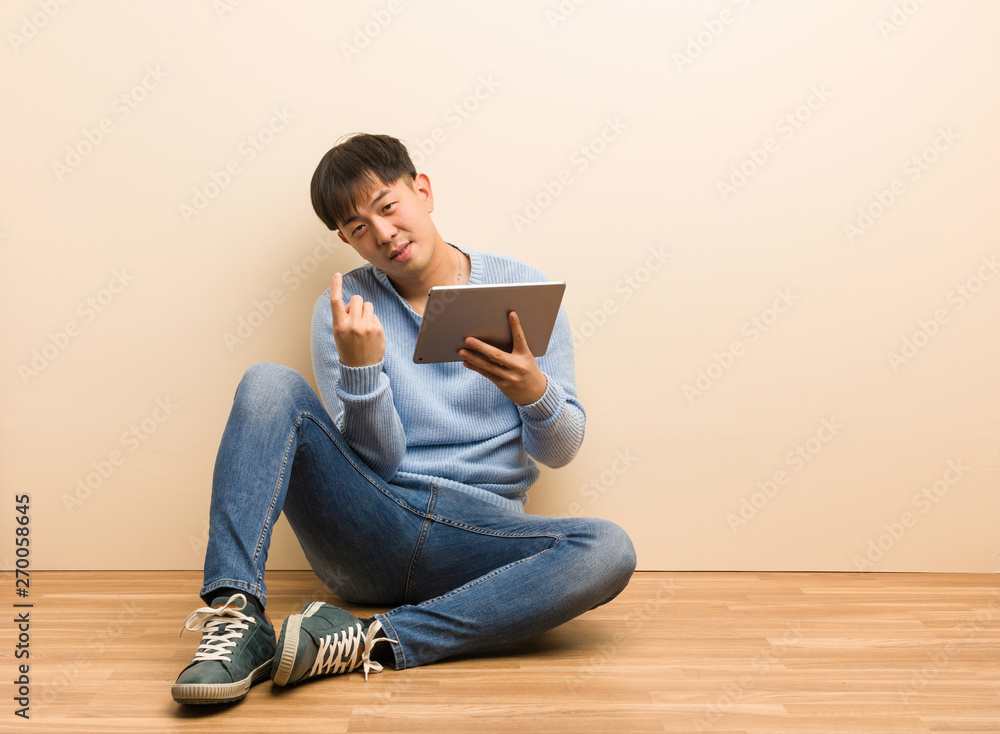 Young chinese man sitting using his tablet inviting to come