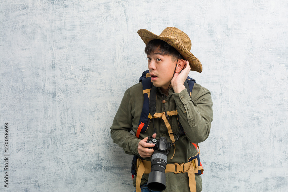 Young chinese explorer man holding a camera try to listening a gossip