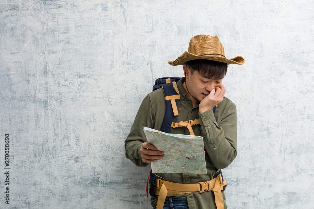 Young chinese explorer man holding a map biting nails, nervous and very anxious
