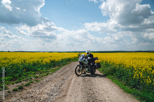 Man extreme sport riding touring enduro motorcycle on dirt. beautiful yellow field of flowers. World adventure rider. Tourist bike. bags equipment, expedition. discovery. summer. Motorcyclist biker