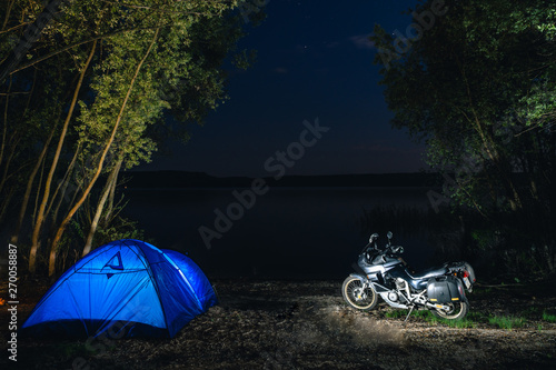 Blue Camping Tent Illuminated Inside. Night Hours Campsite. Recreation. Motorcycle traveler, tourist bikers. lake and stars. take a rest after long riding. Equipment for travel. Campfire, bonfire